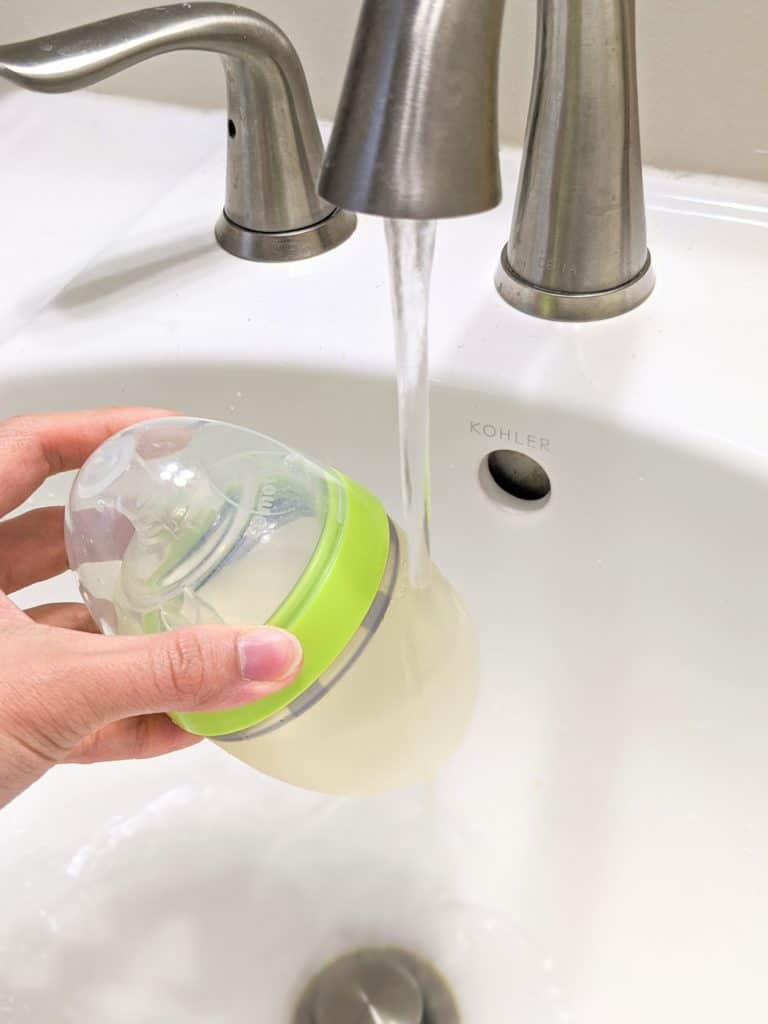 photo of holding baby bottle with milk under warm tap water