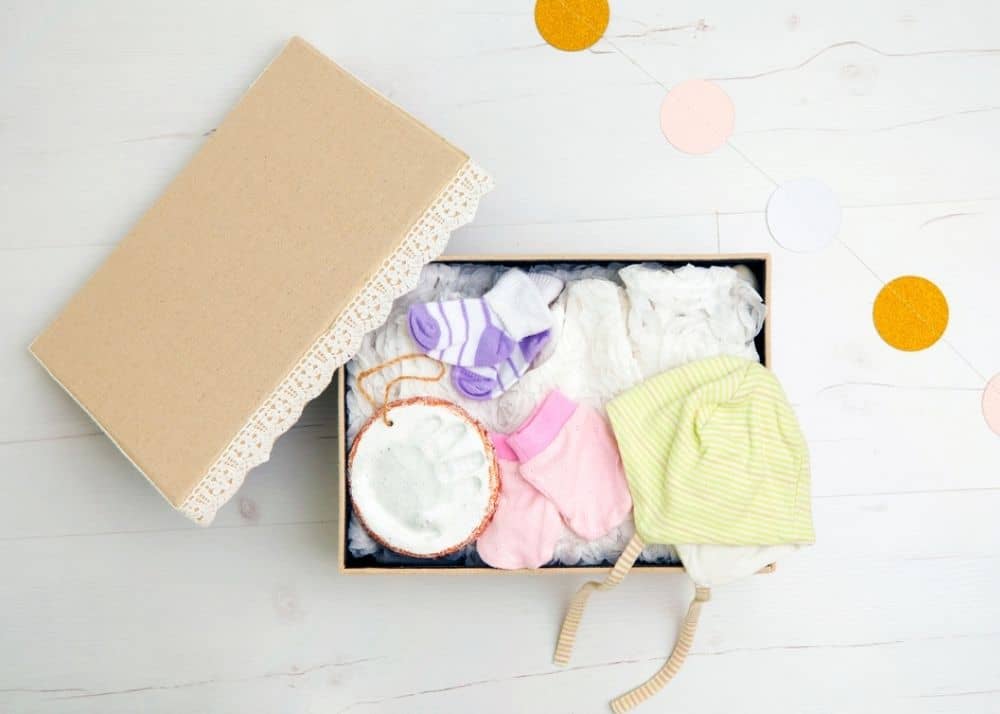 box of baby items, including clothes and handprint ornament