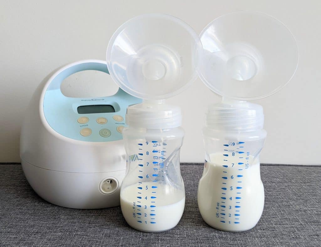 2 breast milk bottles in front of Spectra S1 breast pump showing uneven amount of breast milk and a slacker boob