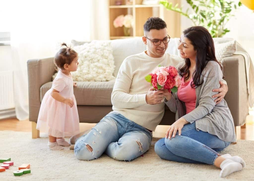 new dad giving new mom push present of flowers with little baby looking on