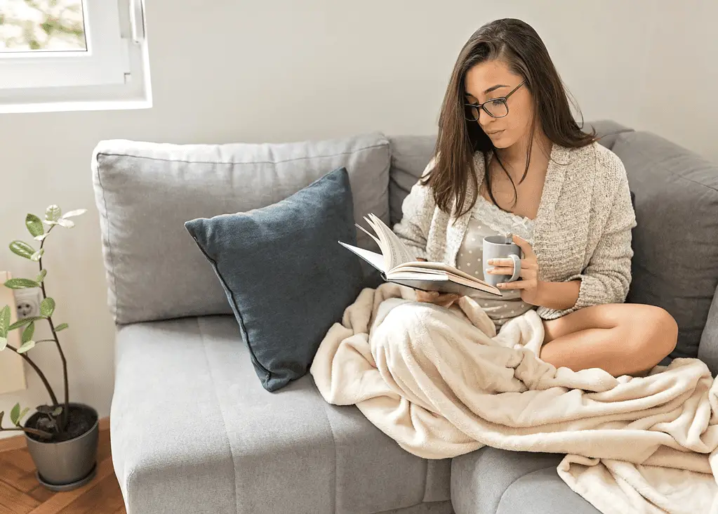 mom snuggled on the couch reading as a hobby while enjoying a hot coffee