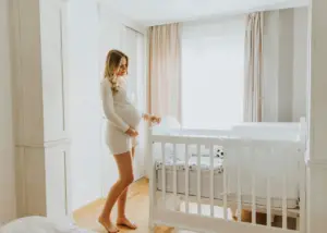 pregnant mom standing over crib in baby's nursery with blackout curtains