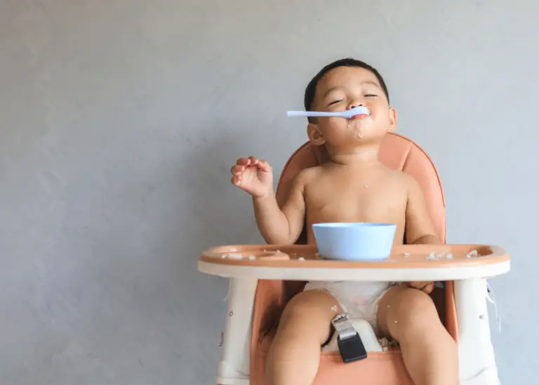 toddler boy in high chair eating hummus with spoon