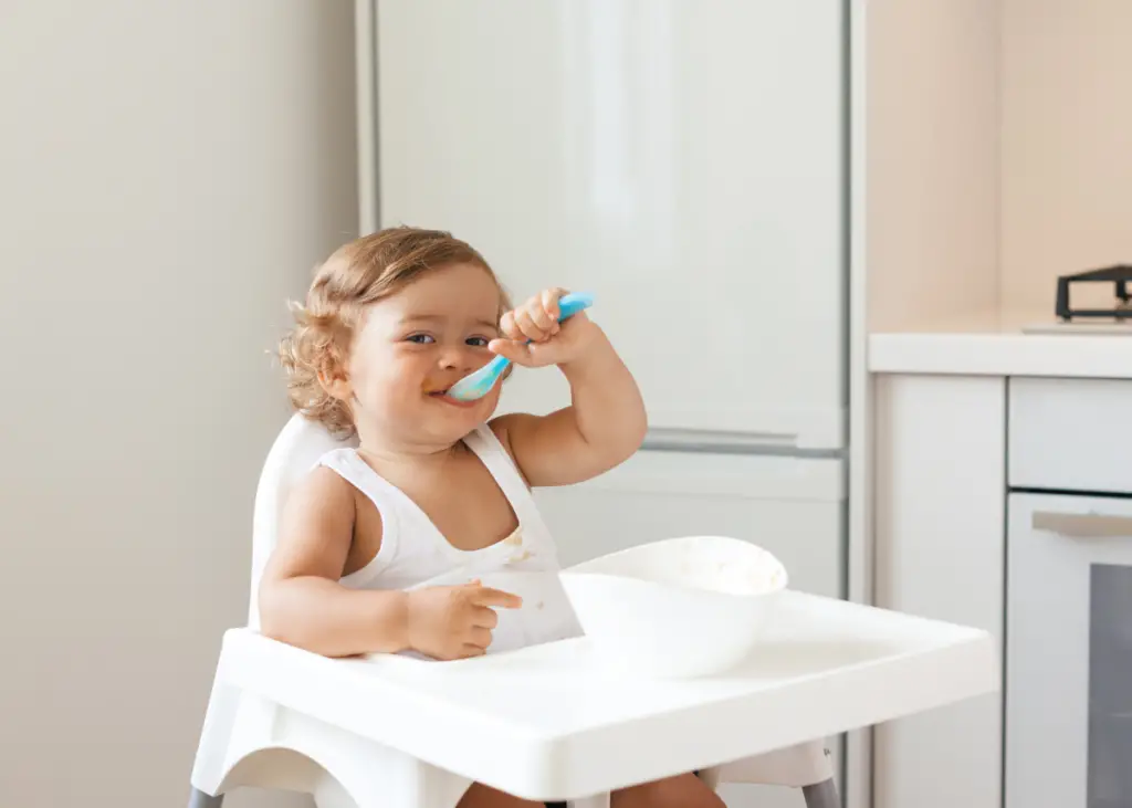 toddler in highchair eating hummus with spoon