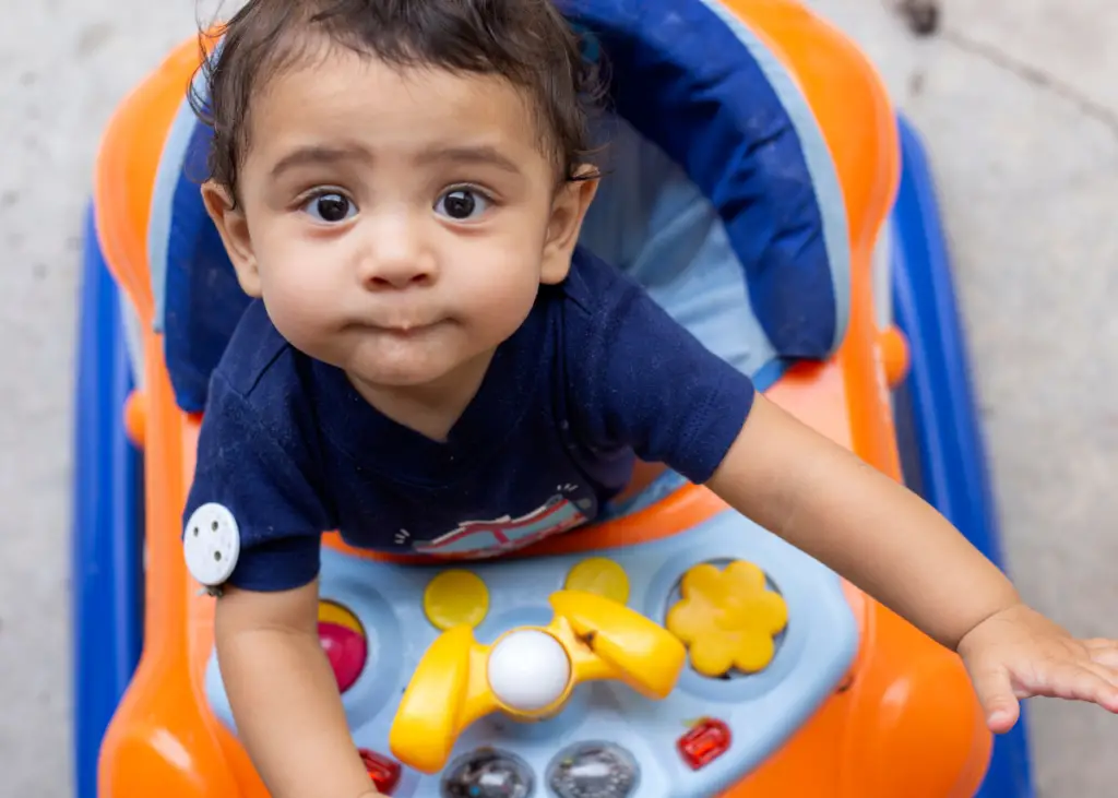 infant sitting in an exersaucer with toys, developing gross motor skills