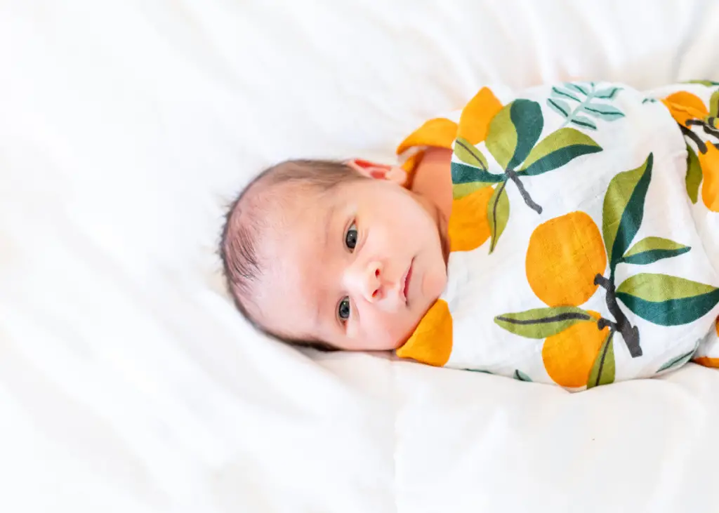 newborn wrapped up in colorful receiving blanket with pattern of oranges