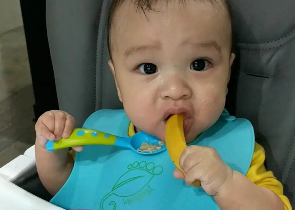 toddler boy enjoying his first mango served in the style of baby-led weaning