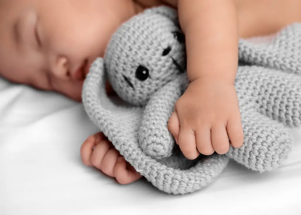 baby sleeping peacefully with warm hands while cuddling stuffy