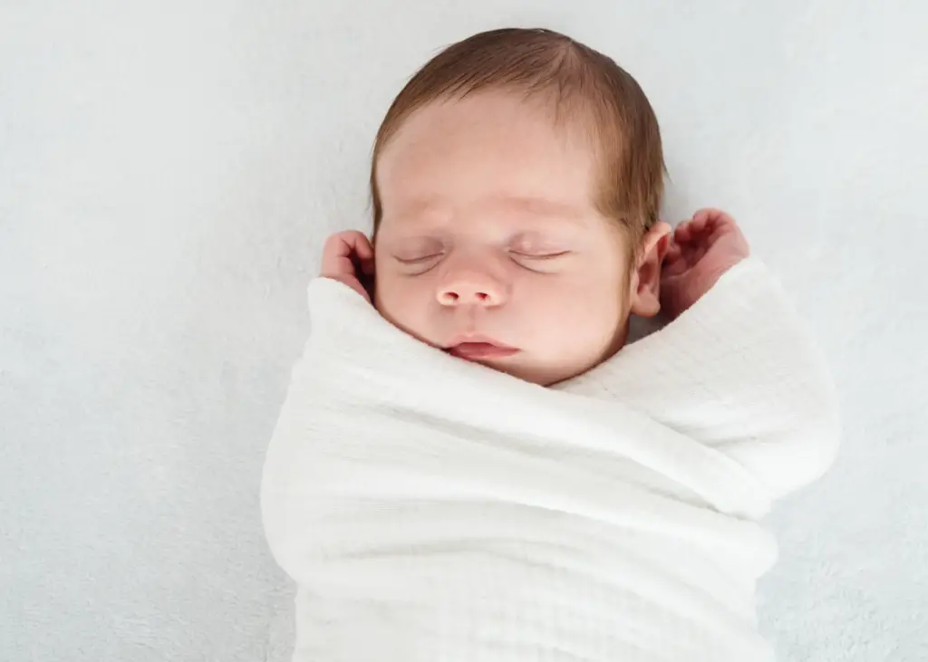 baby sleeping peacefully while swaddled and warm hands