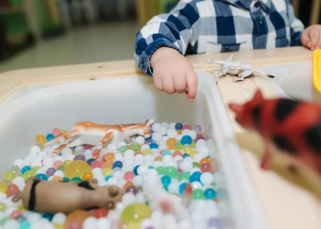 toddler playing with Orbeez water beads in bin with play figurines as part of sensory play