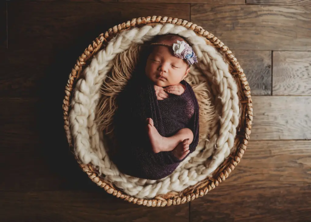 newborn baby girl wrapped in purple swaddle and wearing a flower headband for newborn photoshoot