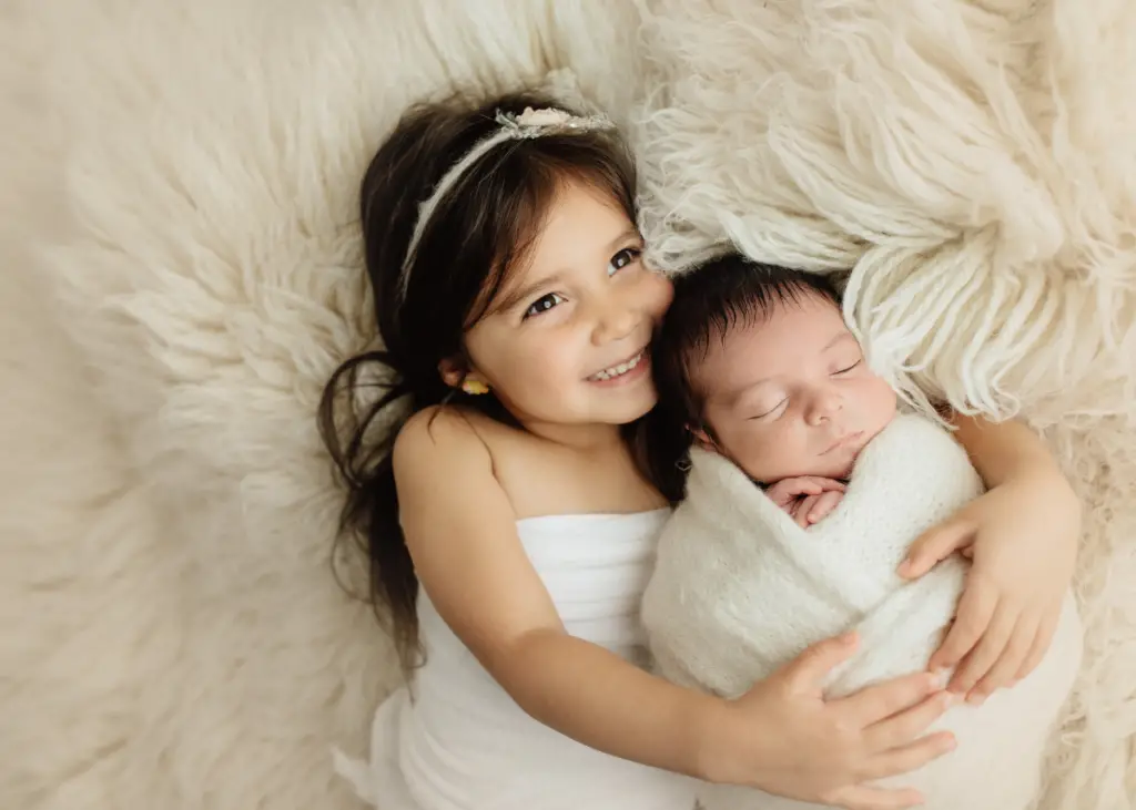 big sister holding newborn baby wrapped in swaddle for newborn photoshoot