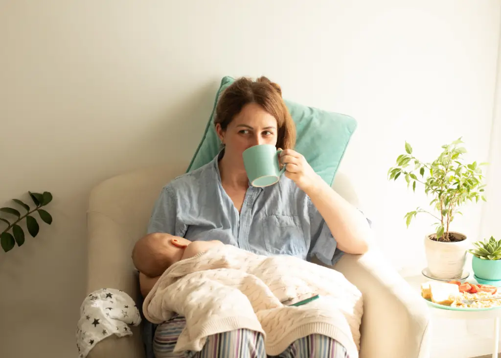 new mom breastfeeding baby drinking herbal tea as one of the best drinks for breastfeeding moms