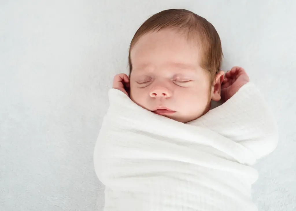 newborn baby wrapped in a white swaddle for a newborn photoshoot