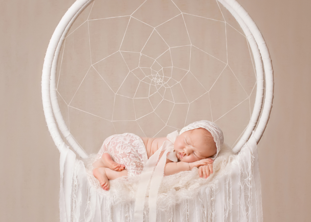newborn baby posing in front of a white dreamcatcher for newborn photoshoot