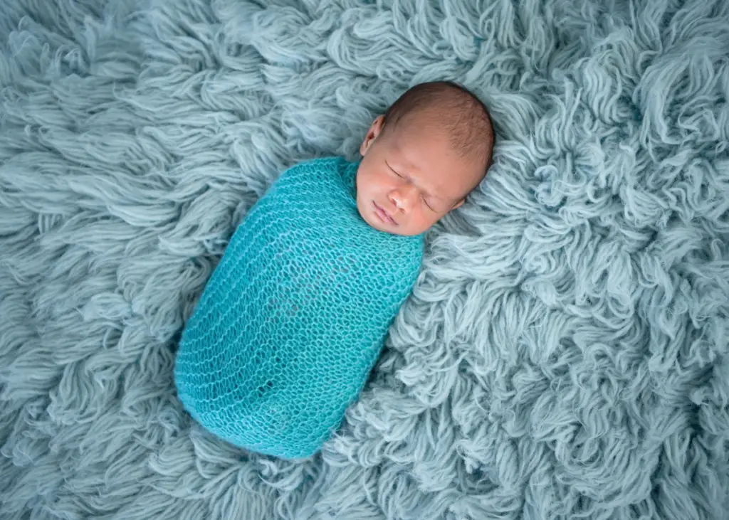 newborn baby wrapped in swaddle on top of a blue carpet for a newborn photoshoot