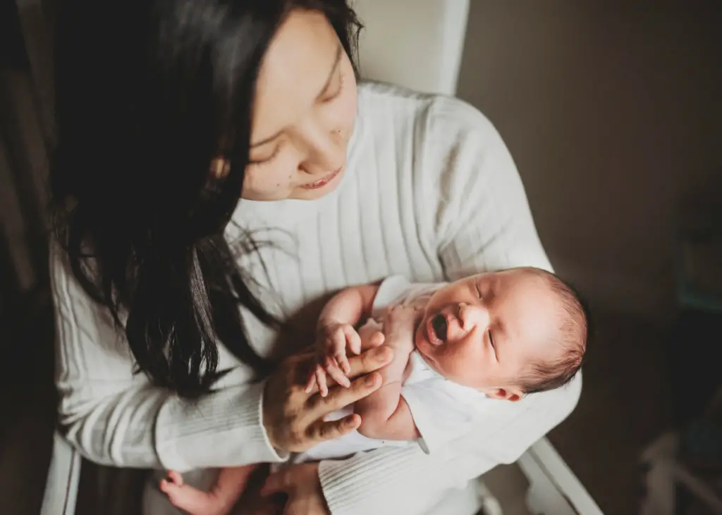 new mom holding newborn baby who is yawning for newborn photoshoot